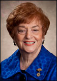 Shirley Asel with short red hair and blue jacket poses, honoring past presidents, against a neutral indoor background.