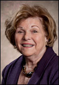 Mary Ann Belin with short brown hair in purple jacket, honored as Past President, wearing a necklace, neutral backdrop.