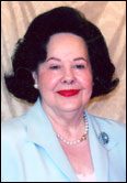 Grace Gandy with dark hair and red lipstick in light blue blazer celebrates legacy of past Guild Presidents indoors.