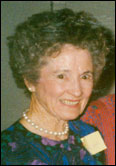 Nell Smith with short curly hair, pearls, and dark patterned top participates in Past Guild Presidents event in university setting.