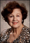Morna Wall with short curly brown hair in leopard print top, honoring past presidents indoors in an academic setting.