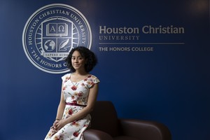 Student in a floral dress sits by Houston Christian University Honors College sign on HCU campus, contemplating future plans.