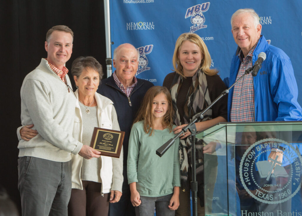Six people, one holding a Family of the Year plaque, stand by a Houston Christian University podium for a group photo.