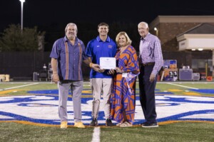 Four adults smile on the HCU campus football field at night, holding a Family of the Year certificate together.
