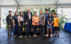 Adults and children from a recognized group smile together inside an event tent with plants, celebrating campus community achievements.