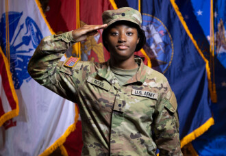 A uniformed U.S. Army soldier salutes near American and military flags on the HCU campus, honoring Military Services.