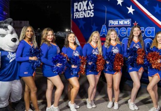 HCU Cheerleaders, mascot, and two hosts pose smiling beside the Fox & Friends America 250 Tour bus on HCU campus.