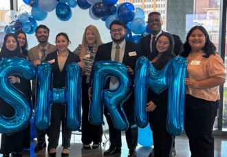 Students smile and hold blue SHRM balloons under an arch at the SHRM Chapter State Competition on the HCU campus.